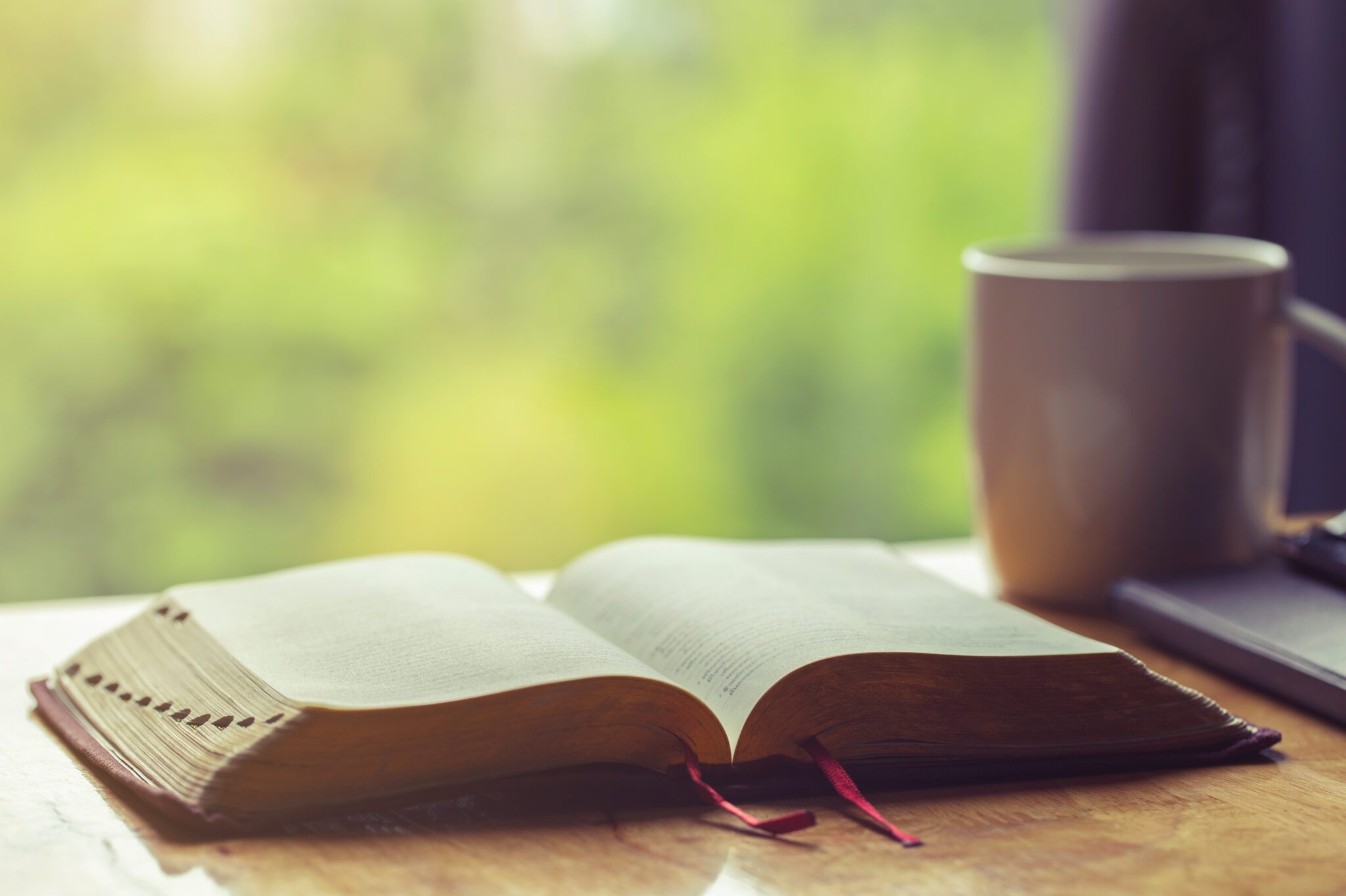 Open bible with a cup of coffee for morning devotion on wooden table with window light